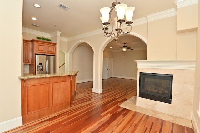 unfurnished living room featuring ceiling fan with notable chandelier, wood finished floors, recessed lighting, crown molding, and arched walkways