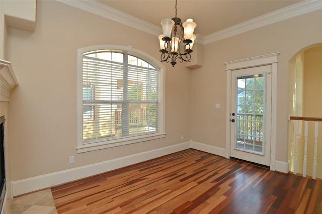 unfurnished dining area featuring an inviting chandelier, wood finished floors, crown molding, baseboards, and arched walkways