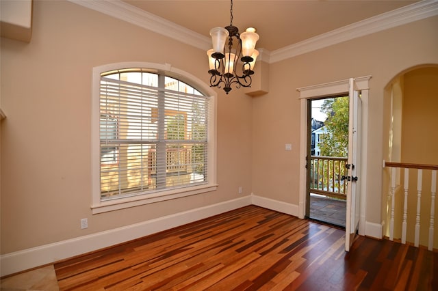 empty room featuring wood finished floors, ornamental molding, a chandelier, arched walkways, and baseboards