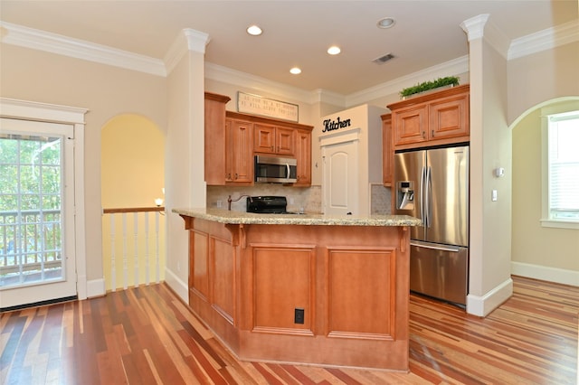 kitchen featuring light wood finished floors, stainless steel appliances, visible vents, arched walkways, and decorative backsplash