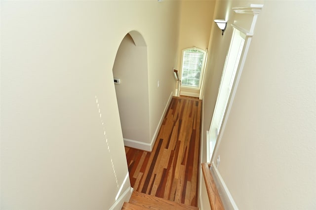 hallway with arched walkways, baseboards, and wood finished floors
