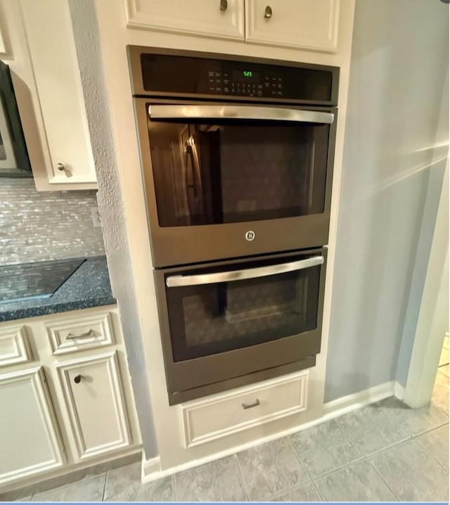 details with baseboards, stainless steel double oven, dark stone counters, black electric cooktop, and tasteful backsplash