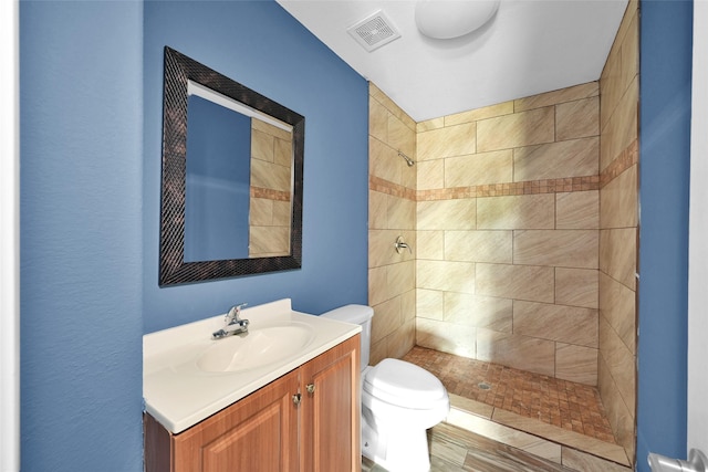 full bathroom featuring vanity, toilet, tiled shower, and visible vents