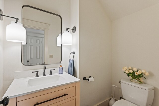half bath with toilet, vanity, and lofted ceiling