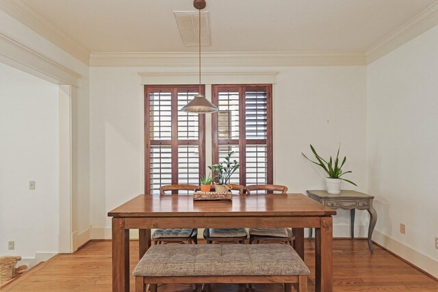 dining space featuring light wood finished floors, crown molding, and baseboards