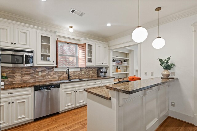 kitchen with appliances with stainless steel finishes, a sink, ornamental molding, light wood-style floors, and a peninsula