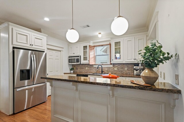 kitchen featuring appliances with stainless steel finishes, a sink, decorative backsplash, glass insert cabinets, and light wood finished floors