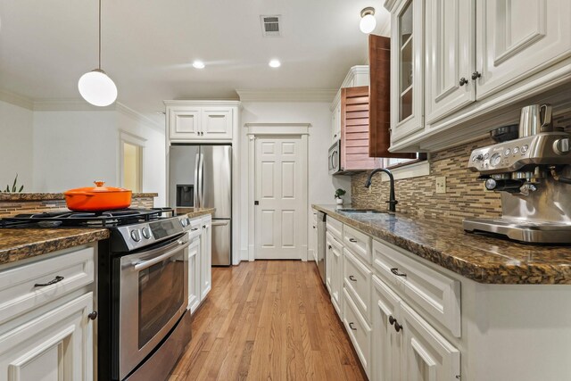 kitchen featuring stainless steel appliances, a sink, crown molding, white cabinets, and backsplash