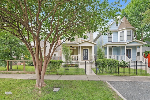 victorian house featuring covered porch, a ceiling fan, roof with shingles, and a gate