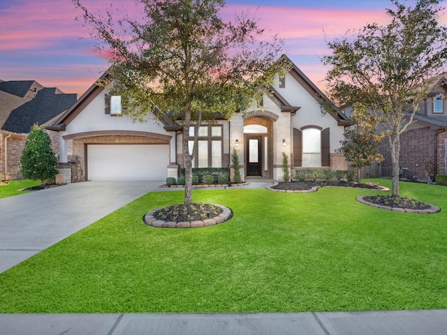 french country style house with a yard, an attached garage, driveway, and brick siding