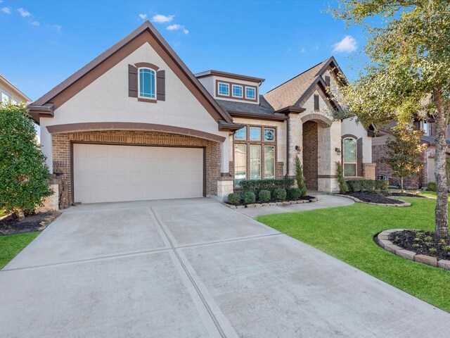 french provincial home with brick siding, driveway, stucco siding, and a front lawn