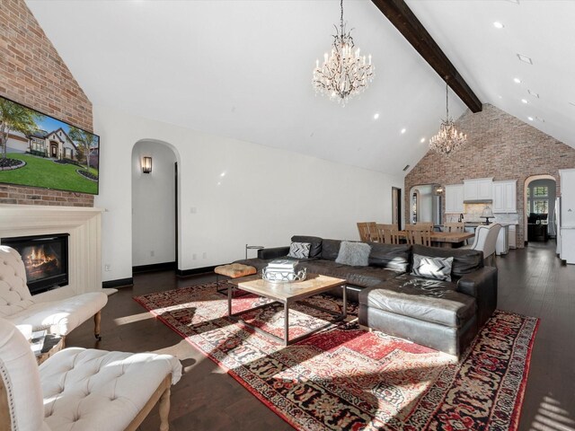 living room with arched walkways, a chandelier, a large fireplace, beamed ceiling, and dark wood finished floors