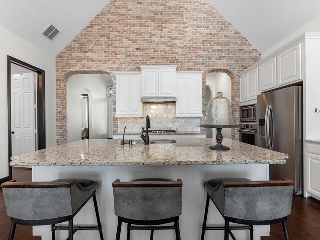 kitchen with vaulted ceiling, appliances with stainless steel finishes, dark wood-type flooring, a sink, and white cabinetry
