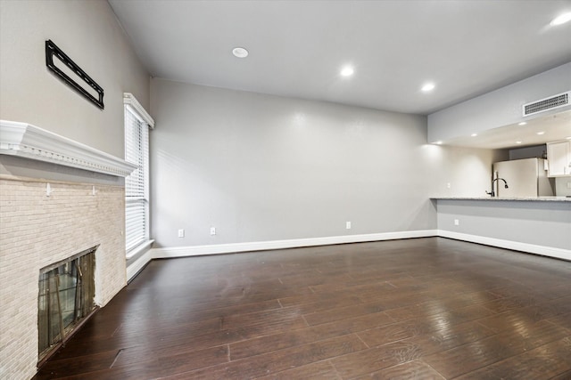 unfurnished living room with a fireplace, dark wood finished floors, visible vents, baseboards, and recessed lighting