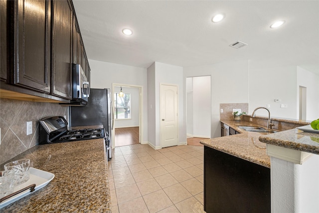 kitchen with a sink, stainless steel microwave, gas range, backsplash, and dark stone counters