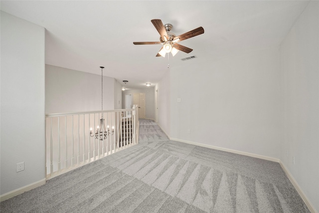 empty room with a chandelier, light colored carpet, a ceiling fan, and baseboards