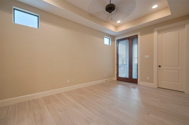 empty room featuring light wood finished floors, a ceiling fan, baseboards, a raised ceiling, and recessed lighting