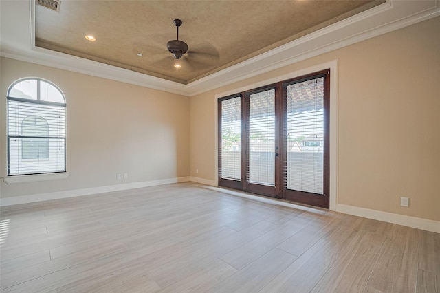 empty room featuring a tray ceiling, crown molding, light wood finished floors, and a ceiling fan