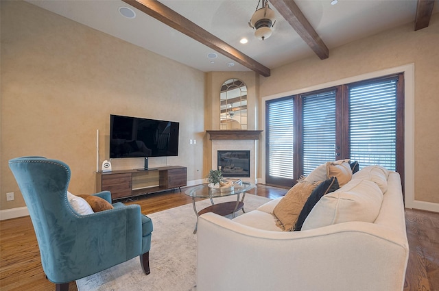 living room featuring baseboards, beamed ceiling, a glass covered fireplace, and wood finished floors