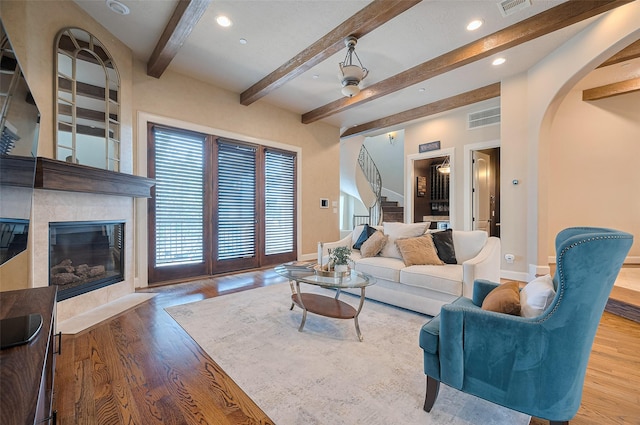 living area with beam ceiling, a fireplace, arched walkways, and stairs
