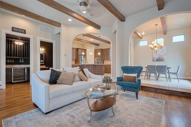 living area with beam ceiling, arched walkways, light wood-style flooring, and beverage cooler
