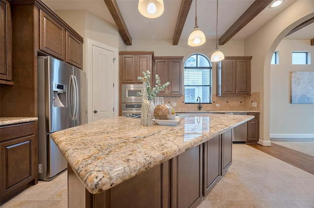 kitchen with beam ceiling, backsplash, arched walkways, a kitchen island, and appliances with stainless steel finishes