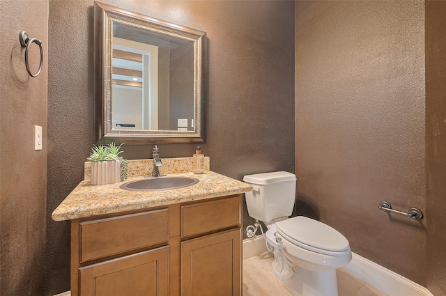bathroom with vanity, toilet, a textured wall, and baseboards