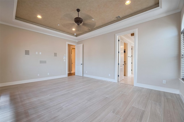empty room with visible vents, crown molding, ceiling fan, a tray ceiling, and baseboards