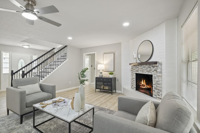 1819 Redwood Ct, Sugar Land, TX 77498 - living room with light wood finished floors, a ceiling fan, a brick fireplace, stairway, and baseboards