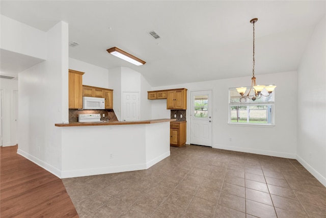 kitchen with white microwave, vaulted ceiling, range, backsplash, and a chandelier