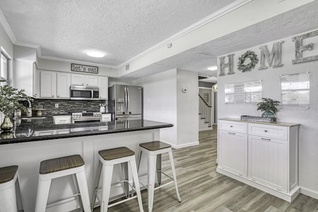 1985 Eastridge Ln, Madisonville, TX 77864 - kitchen with a peninsula, a textured ceiling, light wood-style flooring, and appliances with stainless steel finishes