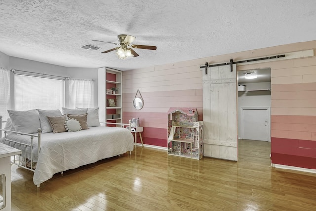 1985 Eastridge Ln, Madisonville, TX 77864 - bedroom featuring wood finished floors, a barn door, visible vents, wooden walls, and baseboards