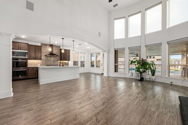 16202 Coyote Run Ln, Cypress, TX 77433 - unfurnished living room with wood finished floors, arched walkways, a towering ceiling, and decorative columns
