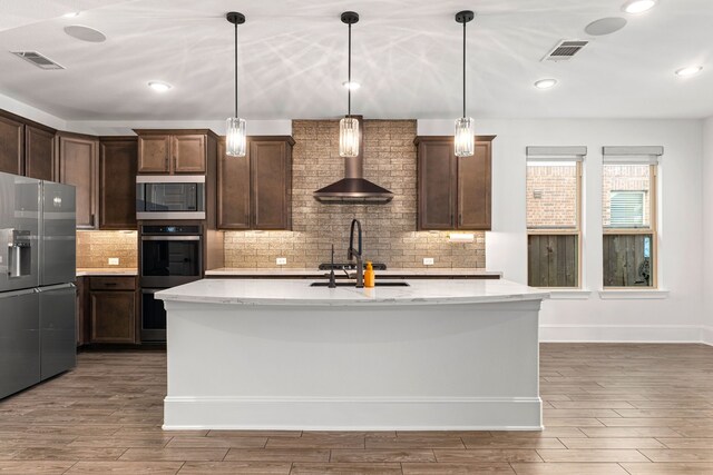 16202 Coyote Run Ln, Cypress, TX 77433 - kitchen with appliances with stainless steel finishes, wall chimney exhaust hood, wood finished floors, backsplash, and dark brown cabinets