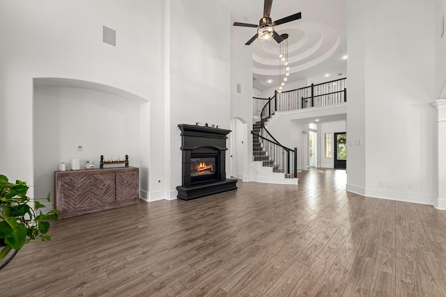16202 Coyote Run Ln, Cypress, TX 77433 - unfurnished living room featuring a glass covered fireplace, a high ceiling, ceiling fan, wood finished floors, and stairway