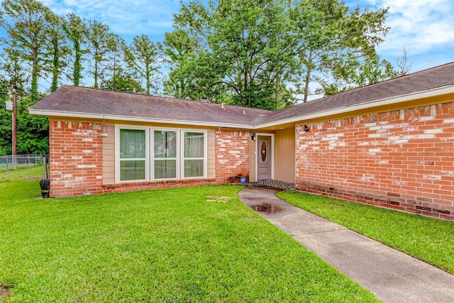 ranch-style house with a front yard, roof with shingles, brick siding, and fence