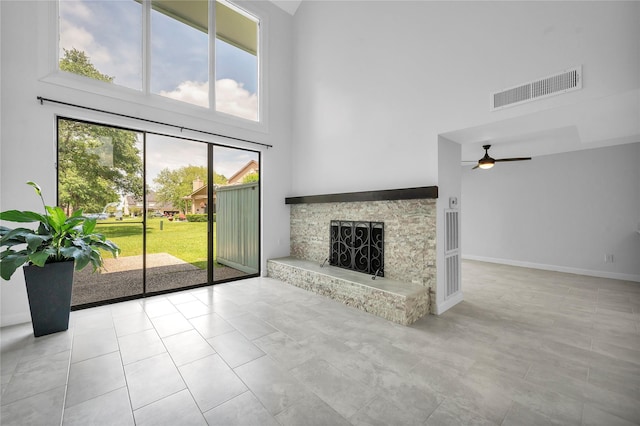 unfurnished living room with baseboards, a stone fireplace, ceiling fan, visible vents, and a towering ceiling