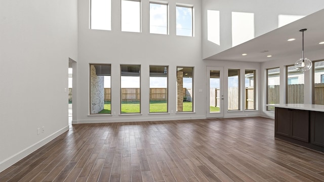 unfurnished living room featuring dark wood finished floors, baseboards, and a towering ceiling