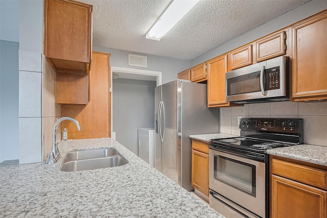 kitchen featuring a sink, tasteful backsplash, a textured ceiling, washer and dryer, and appliances with stainless steel finishes