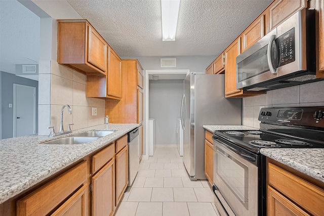 kitchen with a sink, stainless steel appliances, tasteful backsplash, light tile patterned flooring, and light stone counters