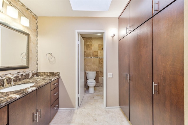 full bath featuring a skylight, toilet, vanity, baseboards, and tile patterned floors