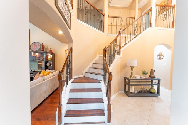stairway featuring arched walkways, a high ceiling, baseboards, and tile patterned flooring