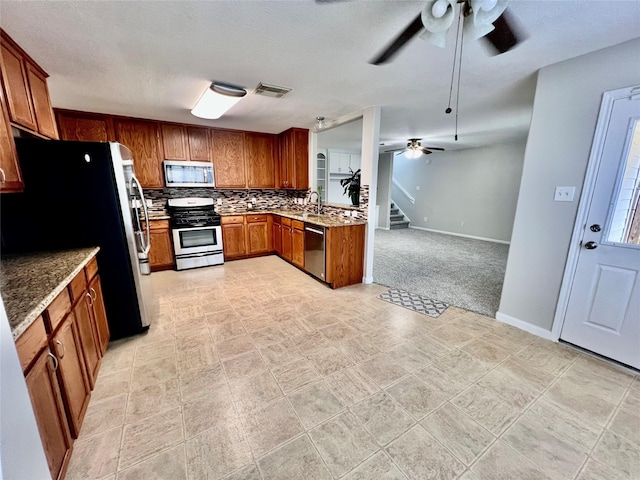 21618 Falvel Lake Dr, Spring, TX 77388 - kitchen with stainless steel appliances, brown cabinetry, visible vents, ceiling fan, and decorative backsplash