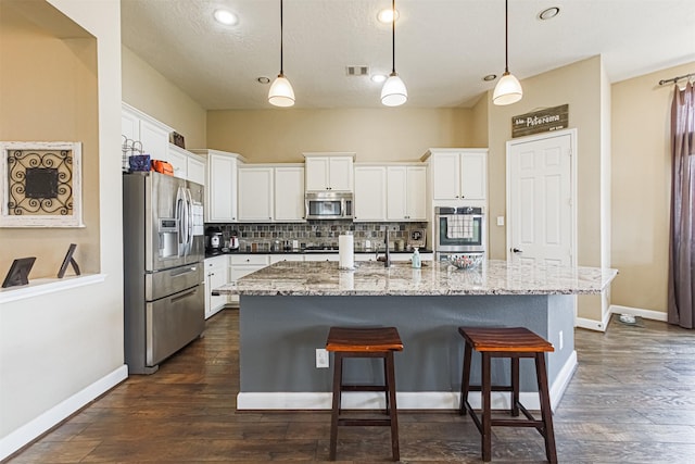 kitchen featuring a breakfast bar, stainless steel appliances, white cabinetry, visible vents, and decorative backsplash