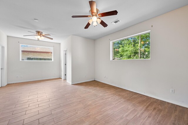 empty room with ceiling fan, light wood-style floors, visible vents, and a wealth of natural light