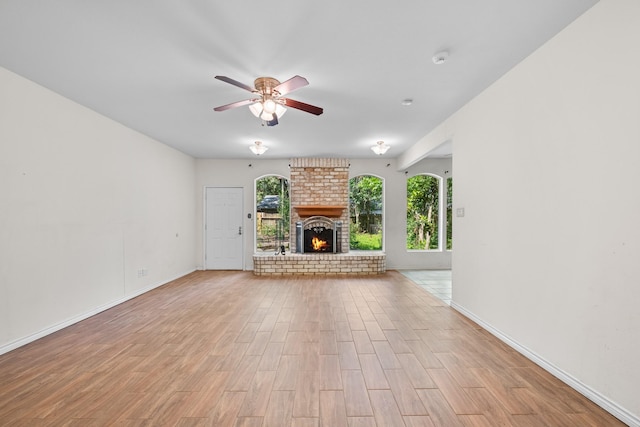 unfurnished living room featuring light wood-style floors, baseboards, a ceiling fan, and a brick fireplace
