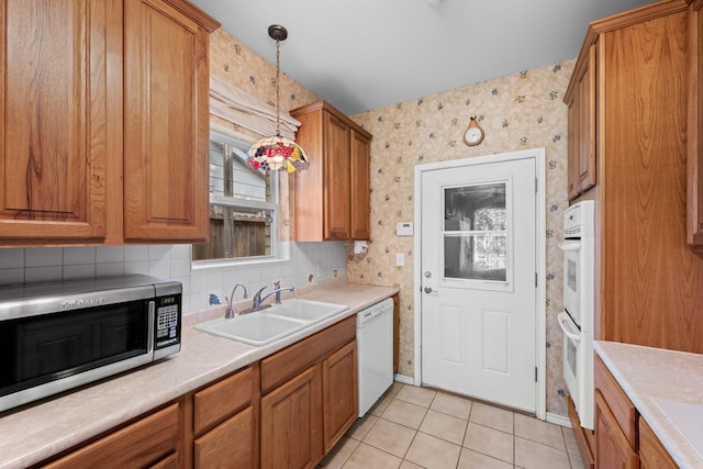 kitchen featuring brown cabinetry, white appliances, wallpapered walls, and a sink
