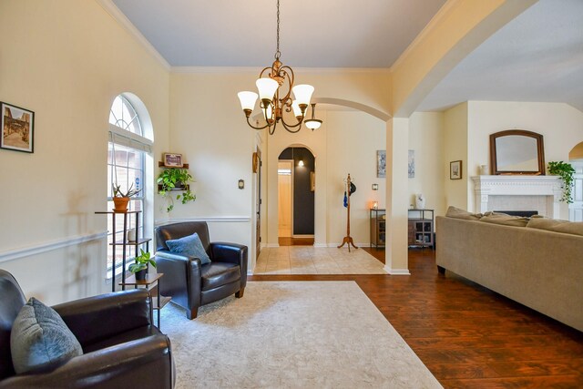 living area with arched walkways, a chandelier, a fireplace, ornamental molding, and wood finished floors