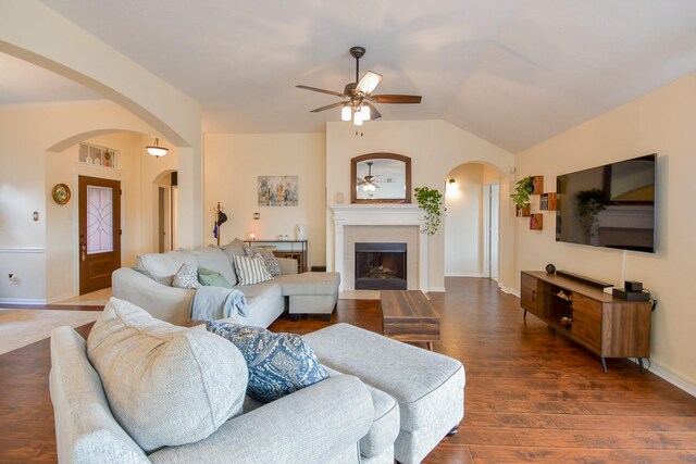 living area featuring ceiling fan, arched walkways, vaulted ceiling, a tiled fireplace, and wood finished floors