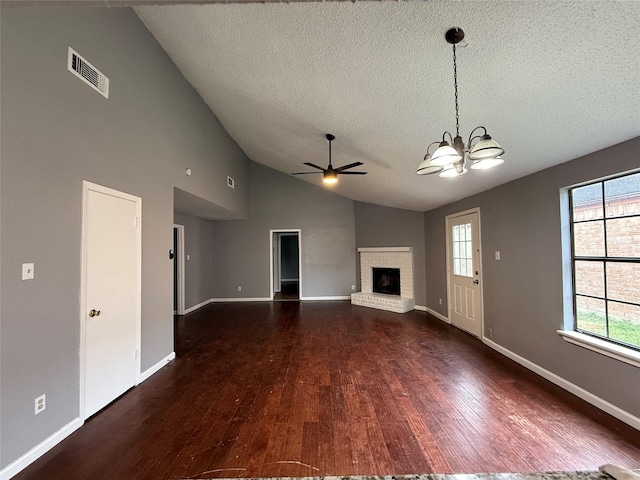 unfurnished living room with wood finished floors, ceiling fan with notable chandelier, a brick fireplace, a textured ceiling, and visible vents